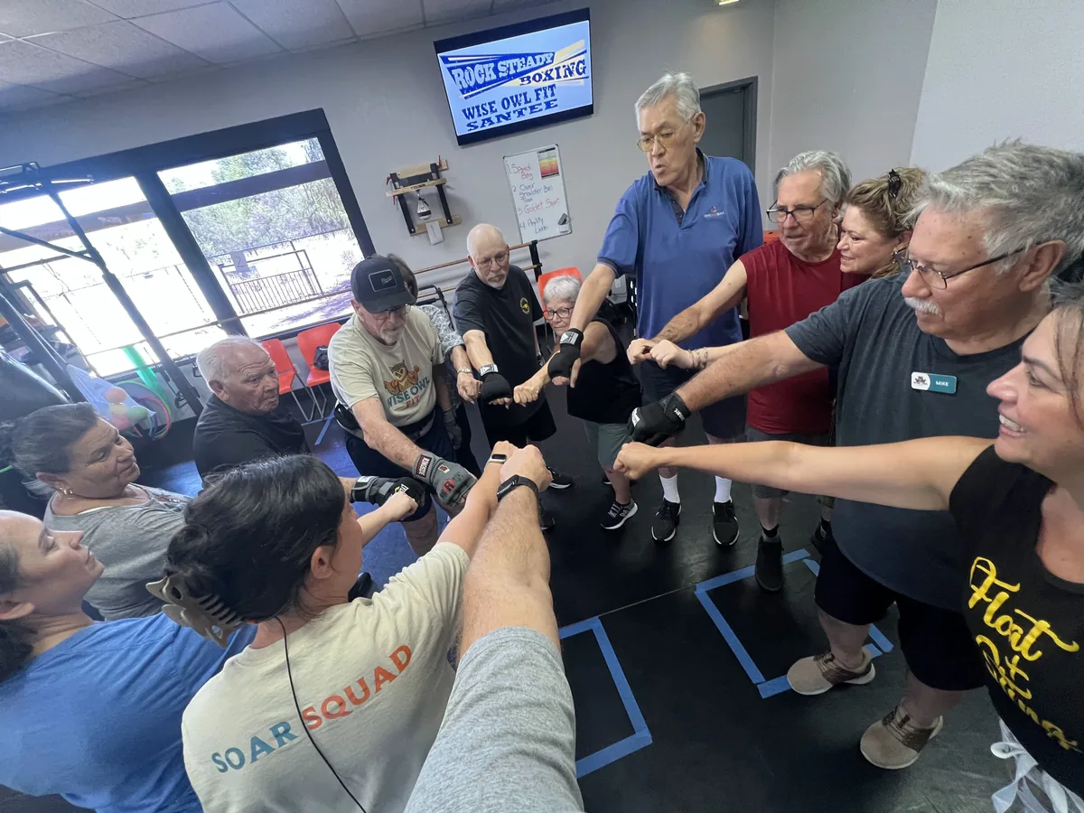 Rock Steady Boxing members in a fist-bump huddle under the Wise Owl Fit Santee banner
